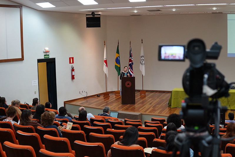 Câmera em primeiro plano e palestra durante simpósio internacional ao fundo